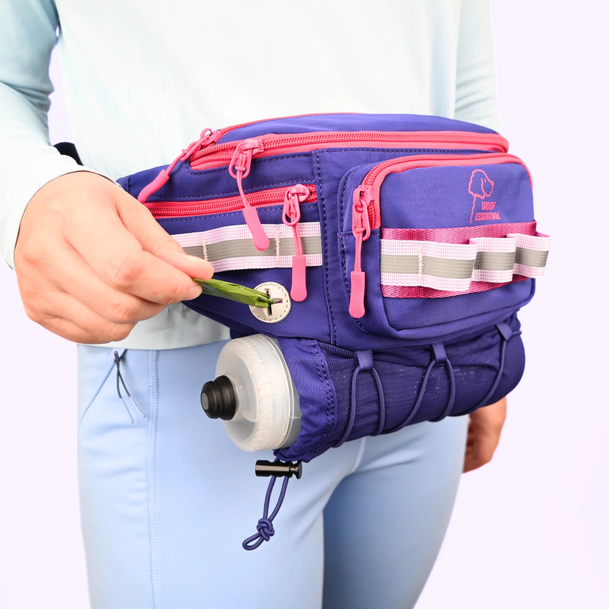 Purple waist bag with pink accents held by a person, featuring a water bottle attachment.