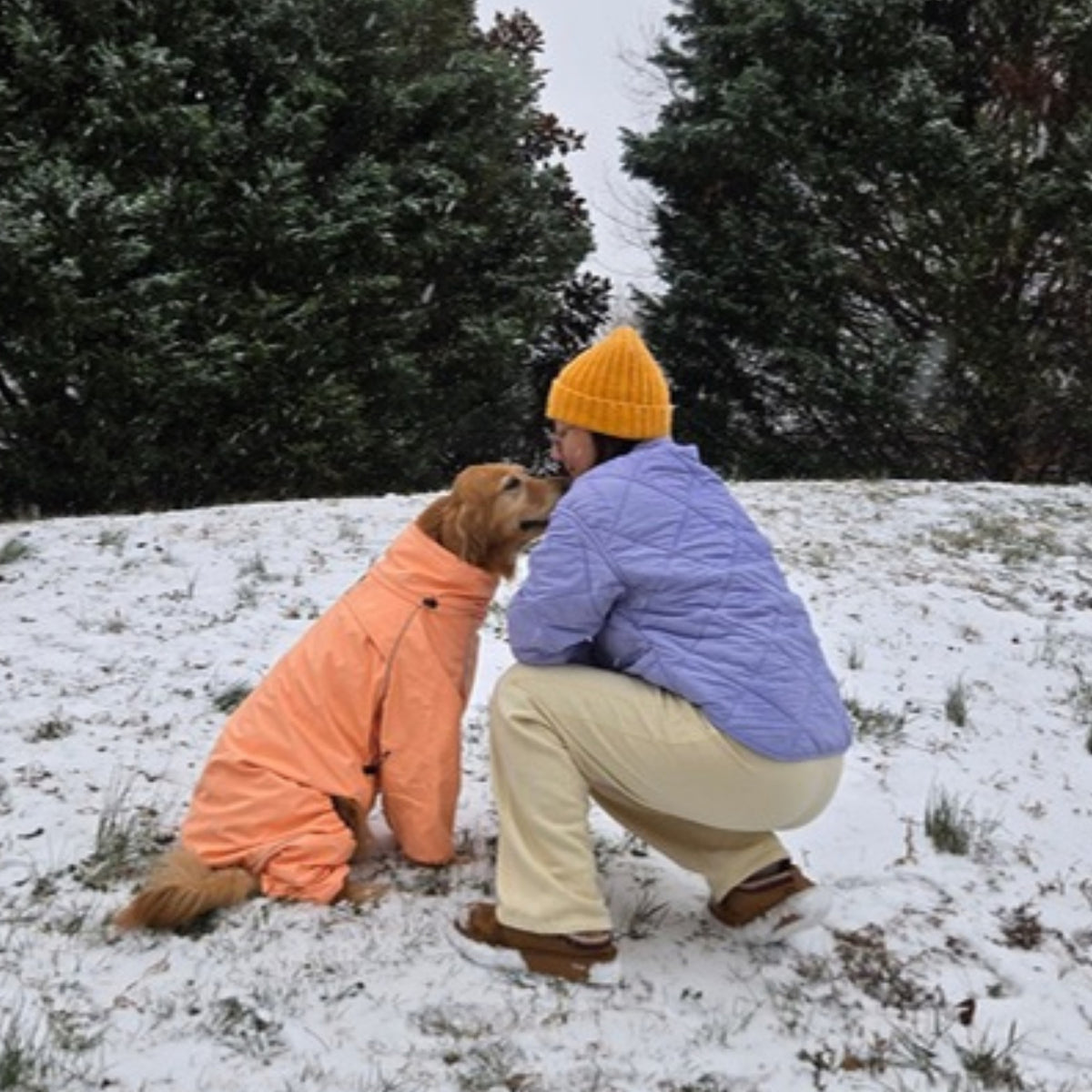 Owner in a Sunset beanie hugging her golden retriever in the Sunset snowsuit in the snow
