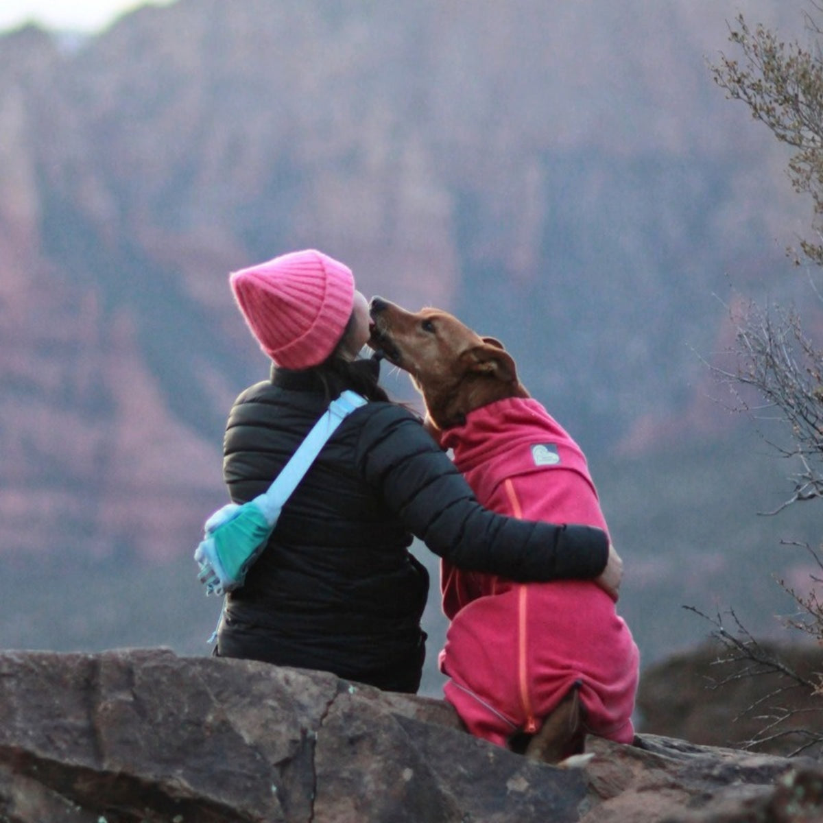 Owner in a pink beanie hugging her dog in the Blossom fleece on a red-rock lookout