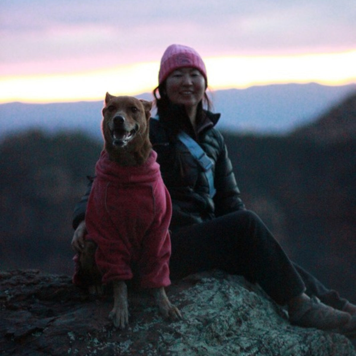 Owner in a pink beanie with her dog in the Blossom fleece on a mountain at dusk