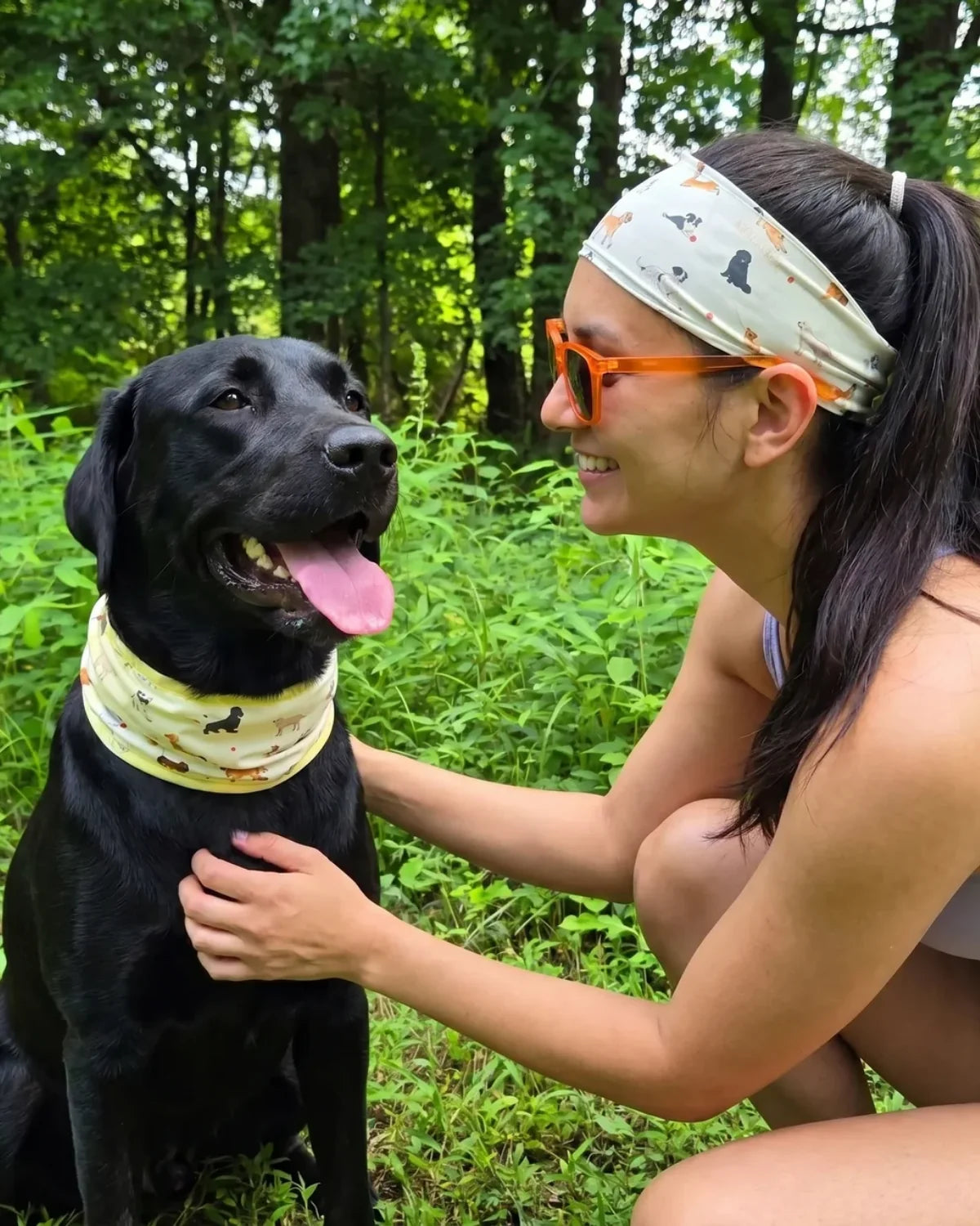 A black Labrador in a dog cooling neck gaiter beside a person wearing the matching cooling headband on a hot day