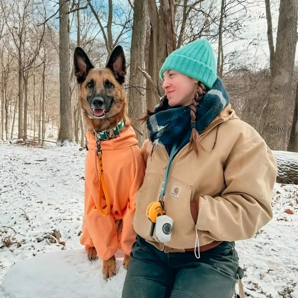 German shepherd in the Sunset snowsuit with its owner in an Oasis beanie on a snowy trail